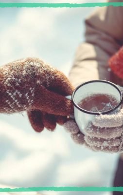 One person giving a warm tea to the other person, both clothed in warm wool clothes and mittens, on a cold winter day, indicating an article on 5 rare herbs that you must have in your winter apothecary to protect your health during wintertime.