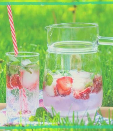 Ice-cold summer cool herbal drinks, with strawberries, put on a grass green background, reflecting an article on best summer cooling herbs for refreshment.